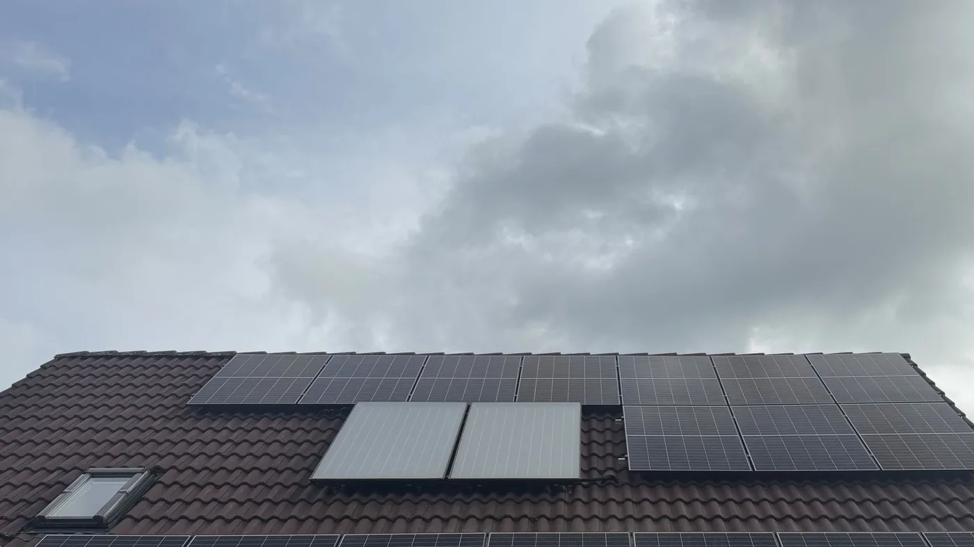 Blick von unten auf ein Satteldach voller Solarmodule vor dramatischem, bewölktem Herbsthimmel