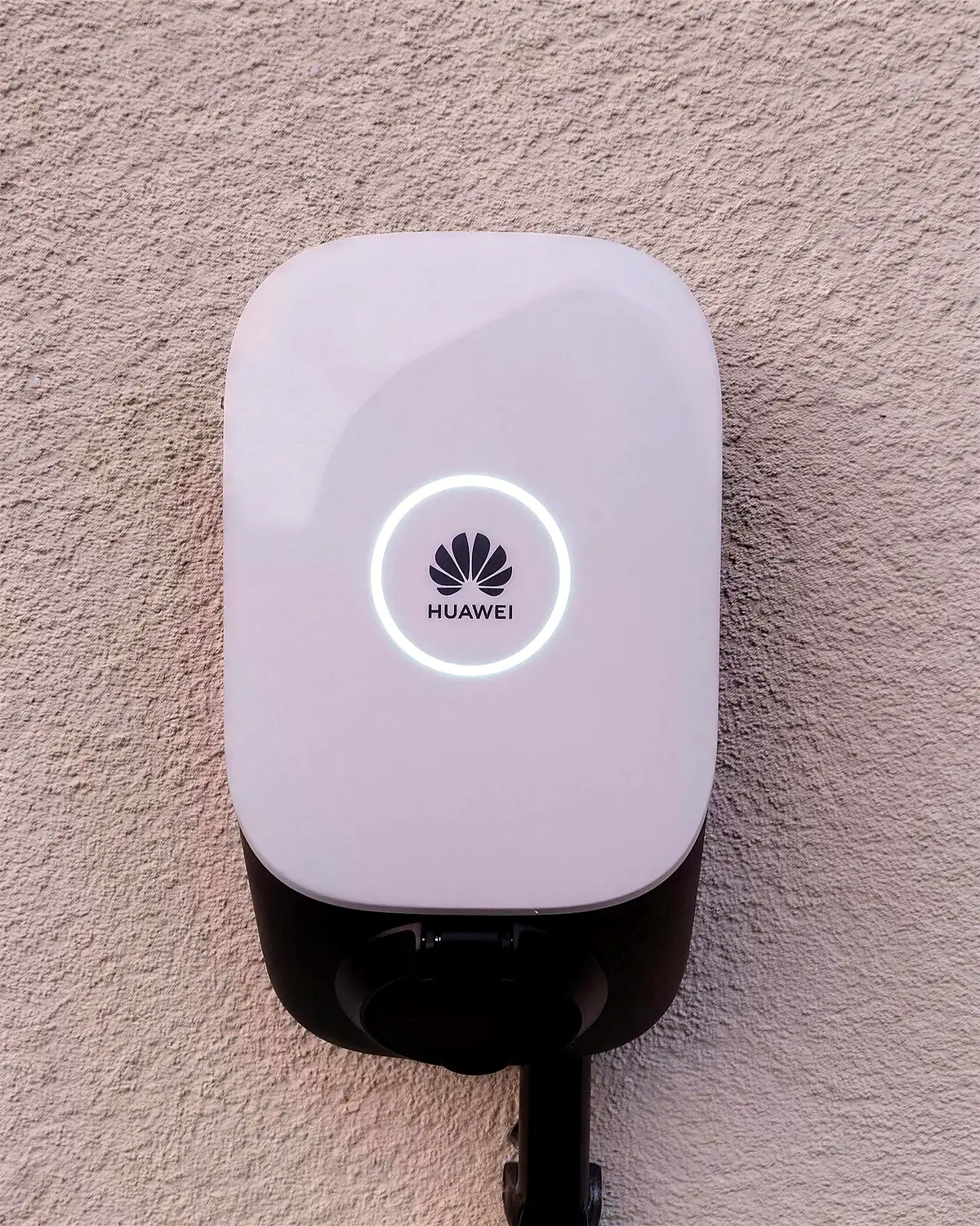 An einer Hauswand montierte Huawei-Wallbox mit beleuchtetem Statusring, angeschlossen über ein sauber verlegtes Steigrohr